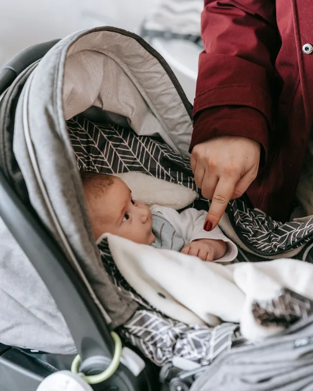 Newborn baby in a winter-wrapped infant carrier looking up at a parent in a red coat